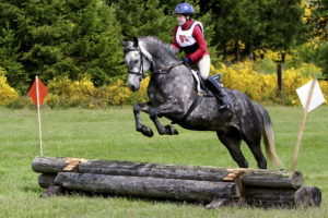 young rider jumping logs at horse trial event